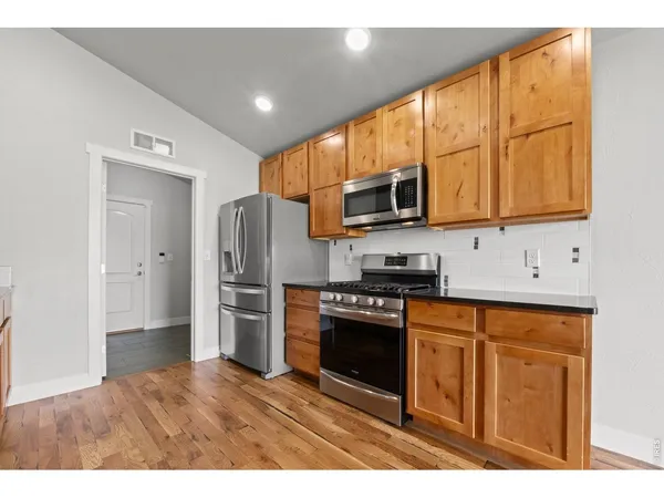 a kitchen with stainless steel appliances granite countertop a refrigerator a sink dishwasher a stove and white countertops with wooden floor