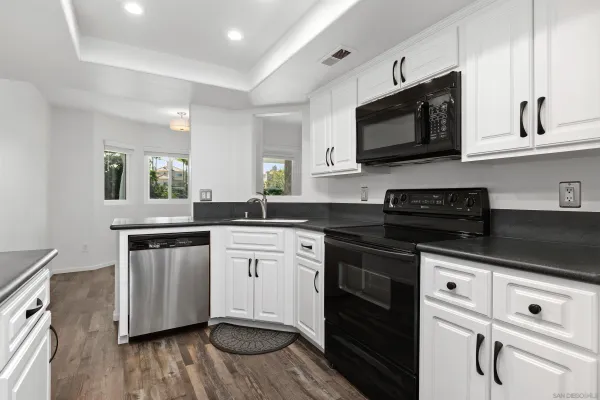 a kitchen with stainless steel appliances white cabinets a sink a stove a microwave and wooden floors