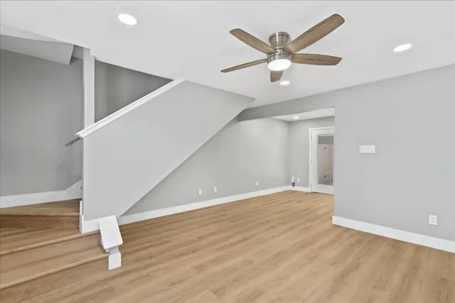 a view of an empty room with wooden floor and a ceiling fan