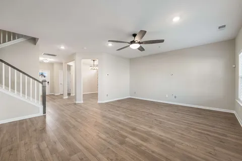a view of an empty room with wooden floor and a ceiling fan