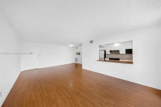 a view of kitchen and empty room with wooden floor
