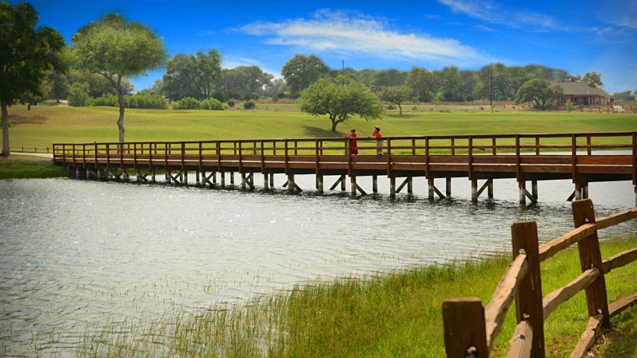128 Hiram Cook Blanco, TX 78606 - Photo 37 of 40 A tranquil lake with a wooden bridge leads to an expansive green landscape under a bright sky.