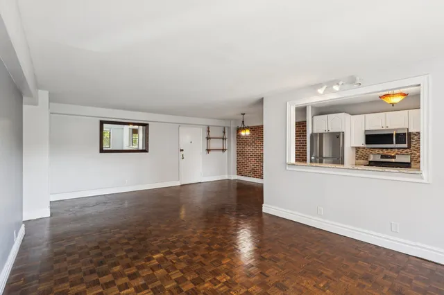 an empty room with wooden floor and kitchen view