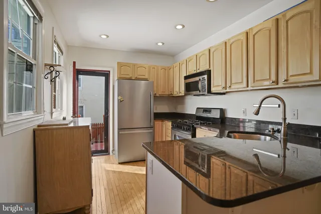 a kitchen with stainless steel appliances granite countertop a sink a stove and a refrigerator with wooden cabinets