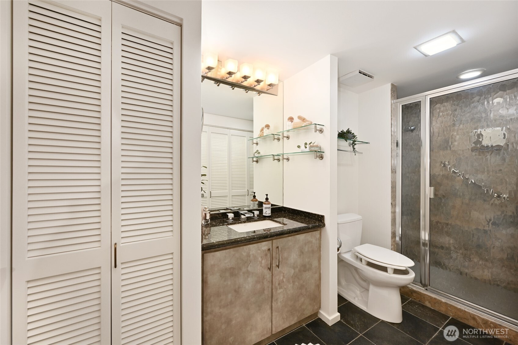 1301 Spring Street, Unit 10F Seattle, WA 98104 - Photo 20 of 36 a bathroom with a granite countertop sink toilet a mirror and shower