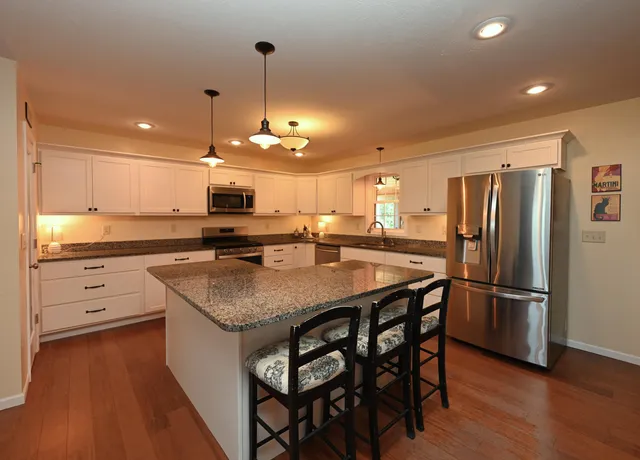 a kitchen with stainless steel appliances granite countertop a refrigerator a sink dishwasher a stove and white cabinets with wooden floor