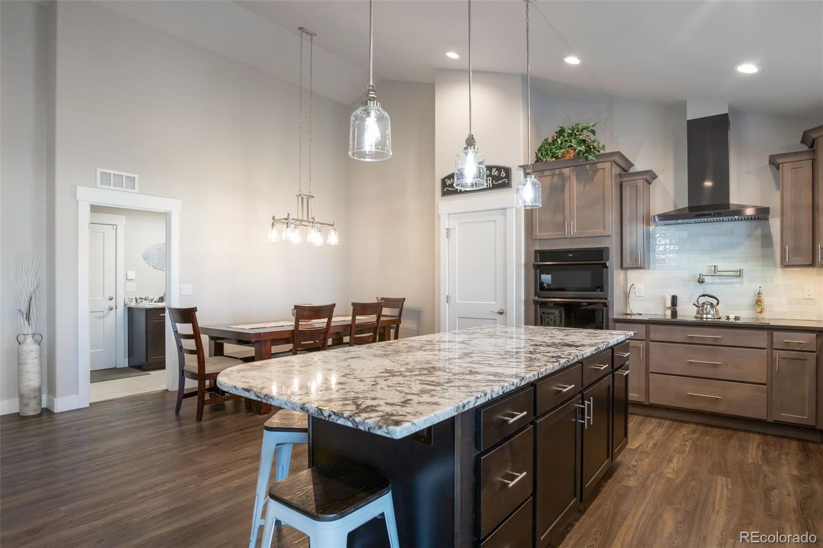3711 Harrier Hawk Road Dacono, CO 80514 - Photo 8 of 40 a kitchen with stainless steel appliances granite countertop a kitchen island a stove a refrigerator a sink a dining table and chairs with wooden floor