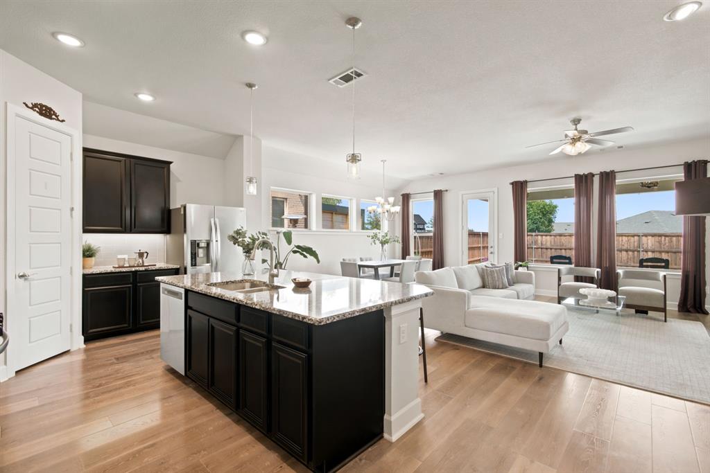 709 Bent Brook Road Oak Point, TX 75068 - Photo 7 of 20 Open-concept living space featuring wood-finish flooring, recessed lighting, a kitchen island with stone countertops and an undermount sink, and black cabinetry with stainless steel appliances