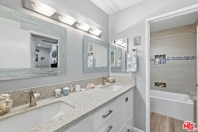 a bathroom with a granite countertop double vanity sink and mirror with bathtub