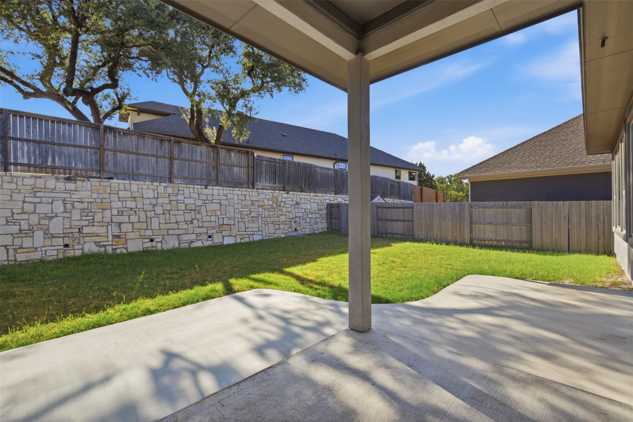 336 Berkeley Place Georgetown, TX 78628 - Photo 28 of 36 A covered concrete patio overlooks a grassy backyard enclosed by wood fencing and stone retaining walls.