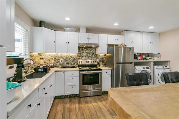a kitchen with refrigerator a stove and white cabinets with wooden floor