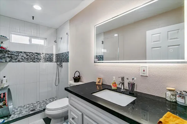 a bathroom with a granite countertop sink a toilet a mirror and shower