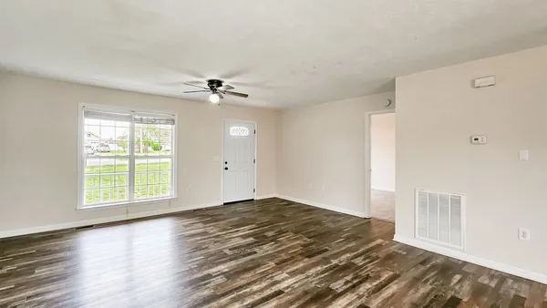 an empty room with wooden floor fan and windows