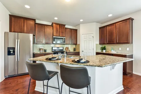 a kitchen with stainless steel appliances granite countertop a stove top oven a refrigerator a sink and a dining table with wooden cabinets
