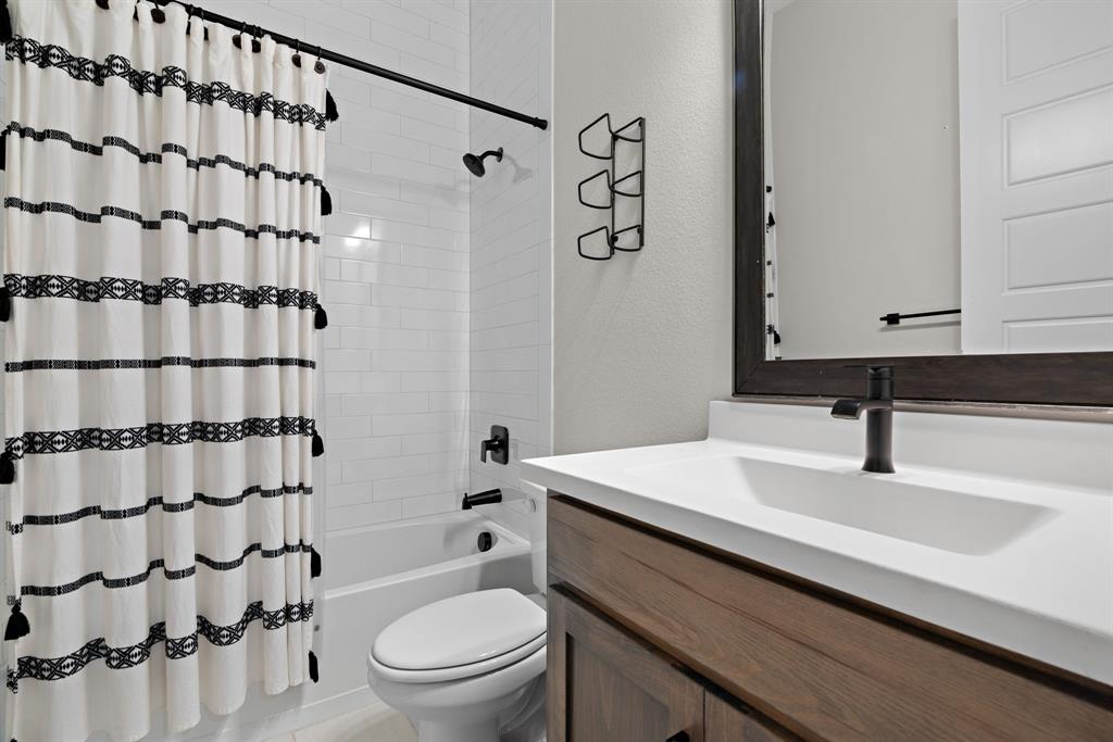 1821 Stonewall Road Argyle, TX 76226 - Photo 25 of 40 Bathroom featuring a white subway tile surround, matte black fixtures, a white vanity countertop with an integrated sink, a wood-finish vanity cabinet, and a framed mirror