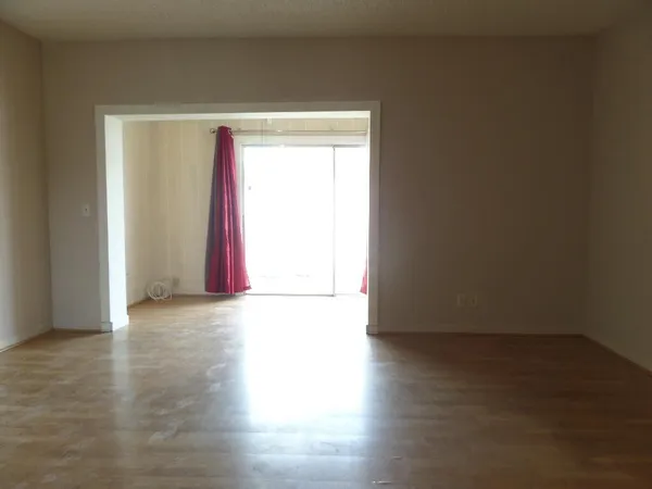 an empty room with wooden floor and windows with curtains
