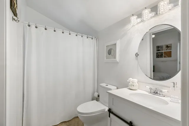 a bathroom with a toilet a sink a mirror a window and vanity