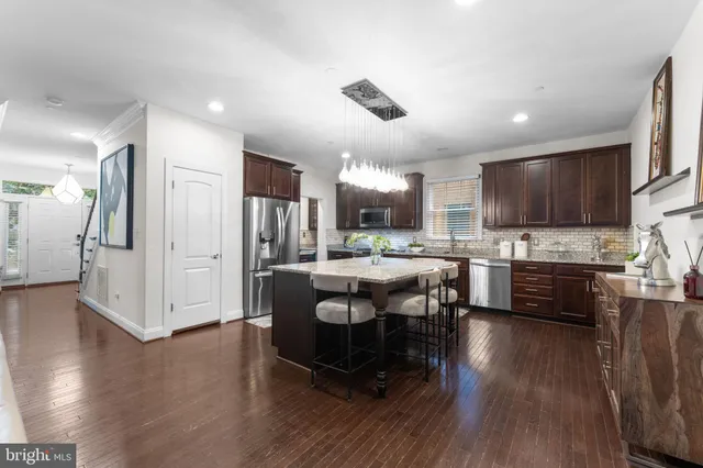 a dining hall with stainless steel appliances kitchen island granite countertop a refrigerator a stove a sink dishwasher a dining table and chairs with wooden floor