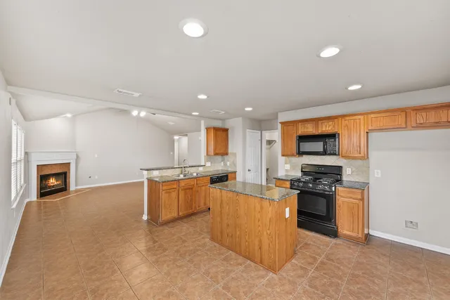 a large kitchen with stainless steel appliances granite countertop a stove top oven a sink dishwasher and a fireplace with wooden floor