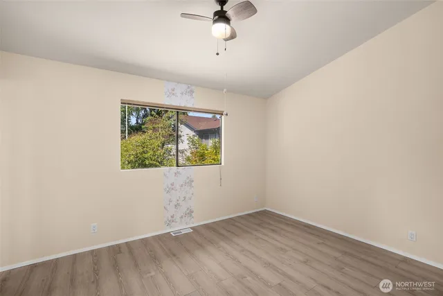 an empty room with wooden floor chandelier fan and windows