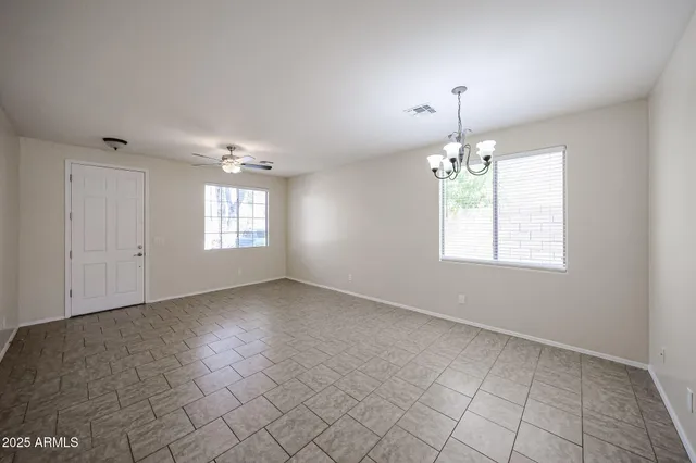 an empty room with chandelier fan and windows