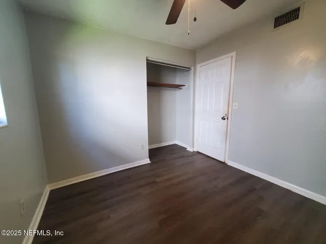 a view of an empty room with wooden floor and a ceiling fan