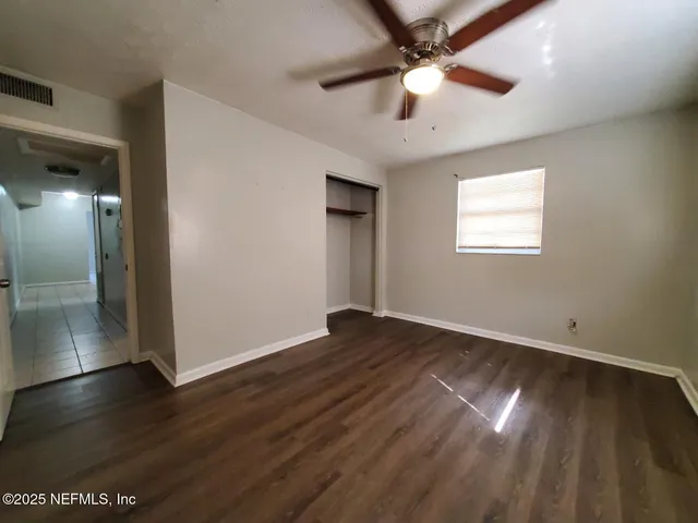 a view of an empty room with wooden floor and a ceiling fan