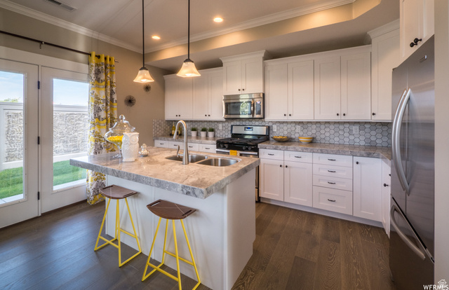 9294 South Rose Cottage Way, Unit 207 Sandy, UT 84094 - Photo 8 of 10 Kitchen featuring white cabinetry, stainless steel appliances, a center island with sink, dark wood finished floors, and crown molding