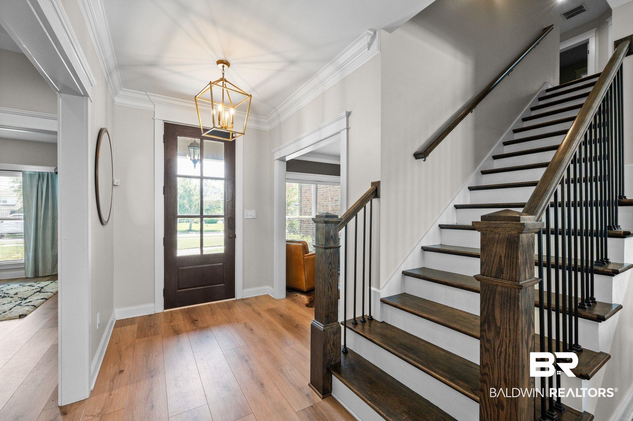 409 Fortune Drive Fairhope, AL 36532 - Photo 3 of 42 Hardwood flooring throughout the entry, featuring a dark wood front door with glass panels, a geometric brass light fixture, and a staircase with dark wood treads and wrought iron balusters