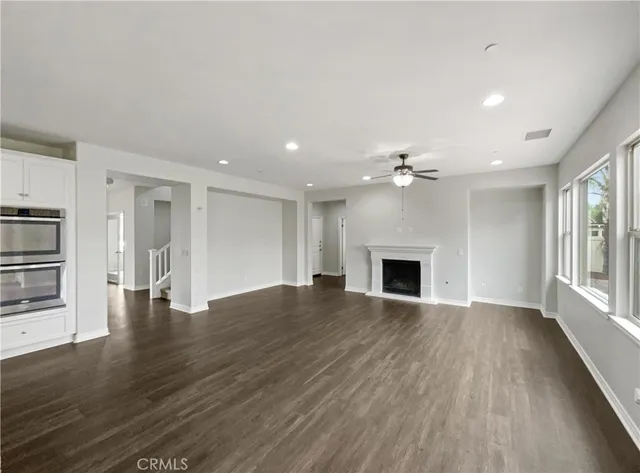 an empty room with wooden floor fireplace and kitchen view