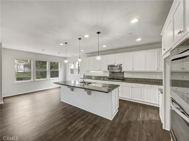 a kitchen with stainless steel appliances granite countertop a stove a sink and white cabinets with wooden floor