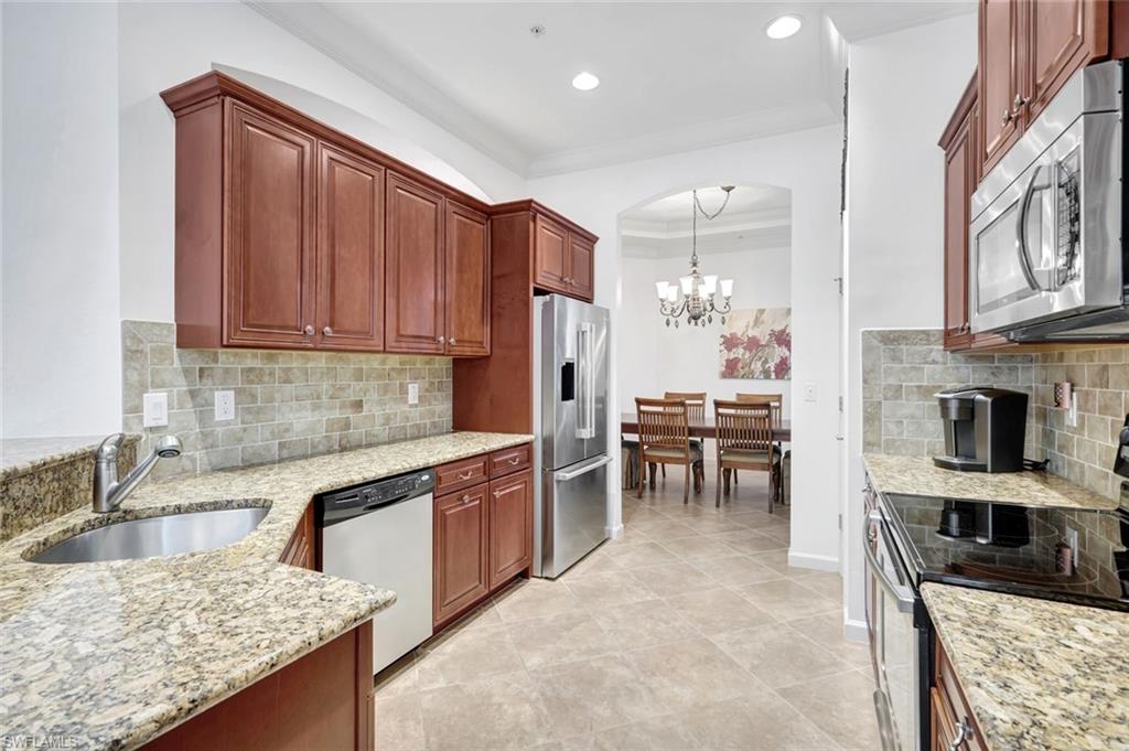 9508 Ironstone Terrace, Unit 201 Naples, FL 34120 - Photo 11 of 45 Kitchen with appliances with stainless steel finishes, tasteful backsplash, light stone counters, decorative light fixtures, and a chandelier