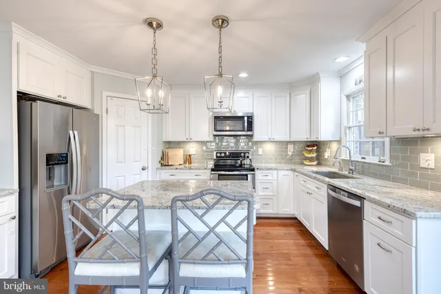 a kitchen with stainless steel appliances granite countertop a refrigerator a sink dishwasher a stove and white cabinets with wooden floor