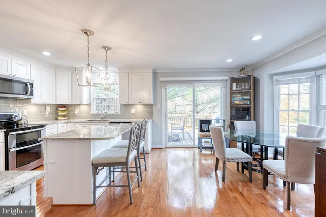 a kitchen with stainless steel appliances granite countertop a stove top oven a refrigerator a dining table and chairs with wooden floor