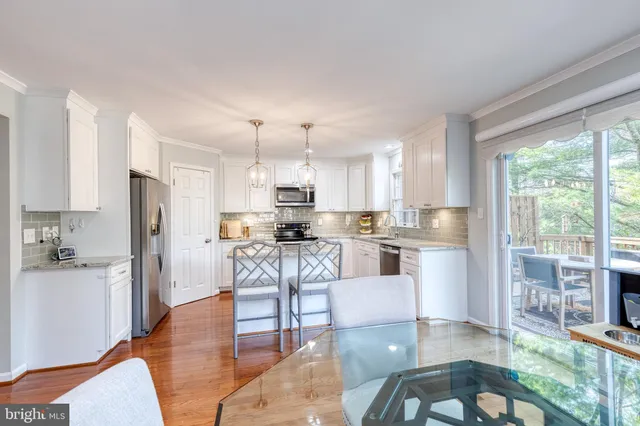 a kitchen with stainless steel appliances kitchen island granite countertop a refrigerator a stove top oven and a dining table with wooden floor