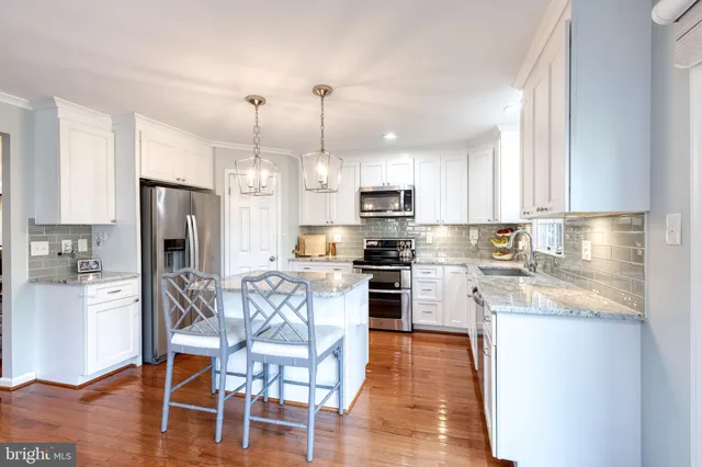 a kitchen with stainless steel appliances granite countertop a stove top oven a refrigerator a sink and a dining table with wooden floor