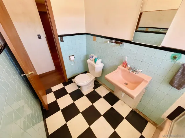 a living room with a black white checkered floor with a gaming machine and dining table