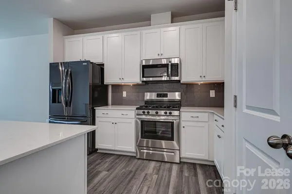 a kitchen with granite countertop a refrigerator stove and white cabinets