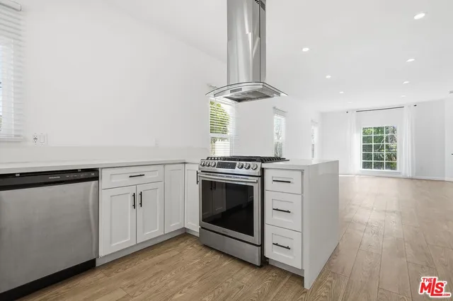 a kitchen with stainless steel appliances a stove and white cabinets with wooden floor