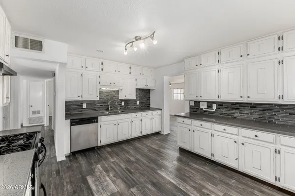 a kitchen with granite countertop white cabinets a sink dishwasher and a stove with wooden floor