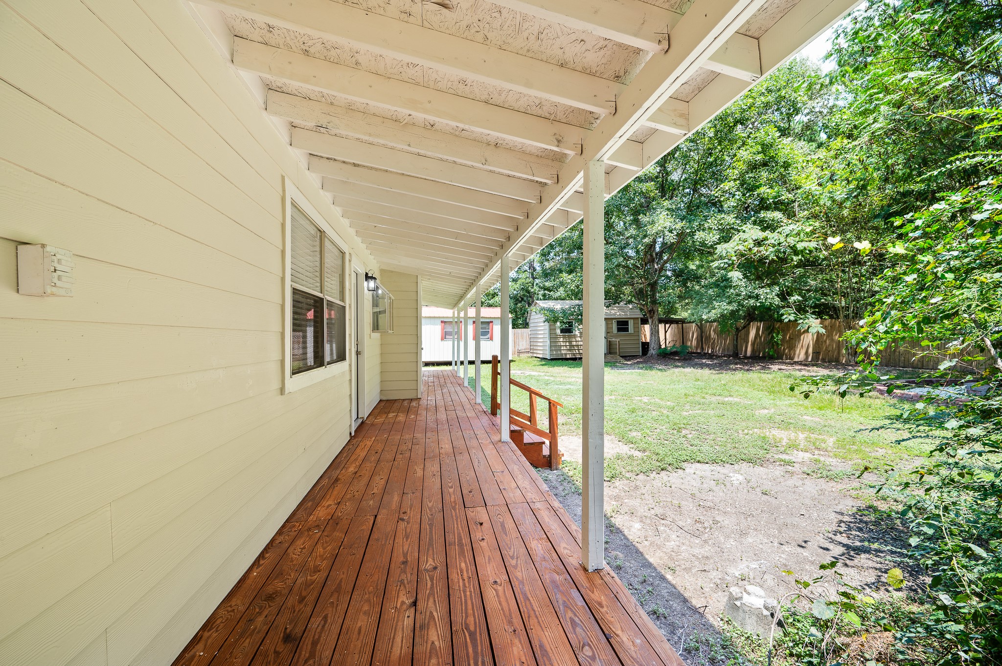 61 Hicks Loop West Cleveland, TX 77328 - Photo 35 of 38 Charming covered porch with rich wooden flooring overlooks a spacious, fenced backyard surrounded by lush greenery.