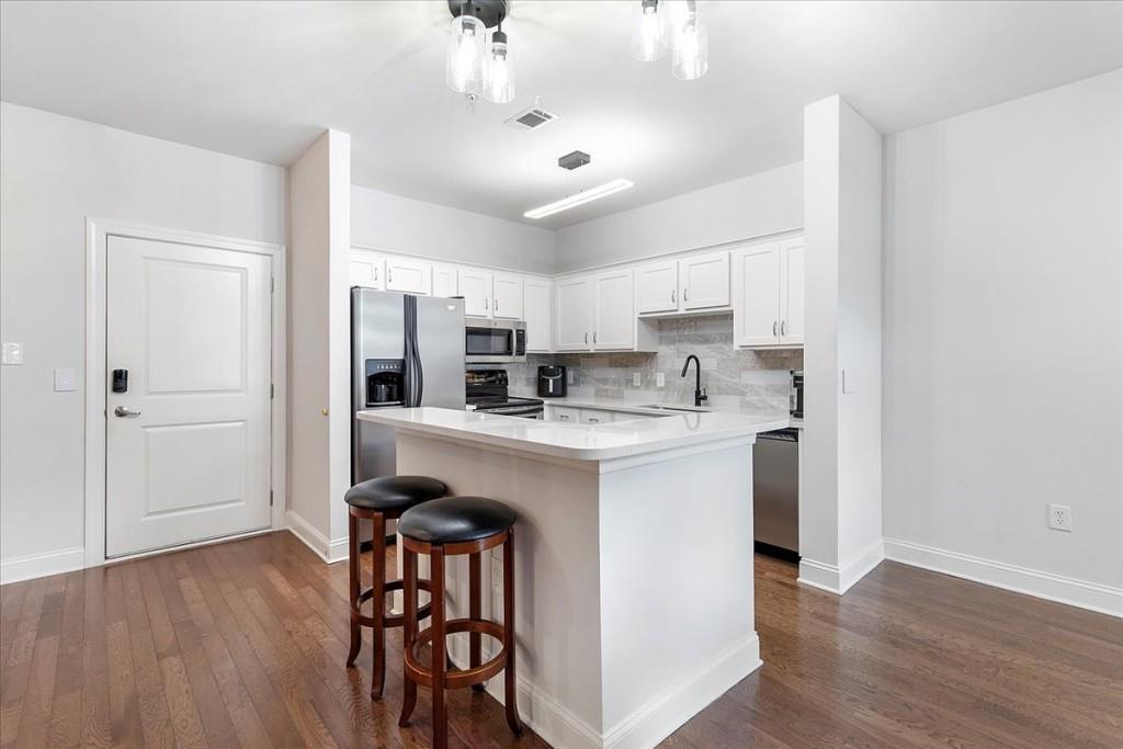 a kitchen with stainless steel appliances granite countertop a white refrigerator a stove a sink dishwasher and white cabinets with wooden floor