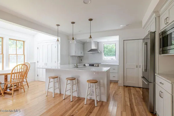 a kitchen with stainless steel appliances granite countertop a stove a refrigerator a sink a dining table and chairs with wooden floor