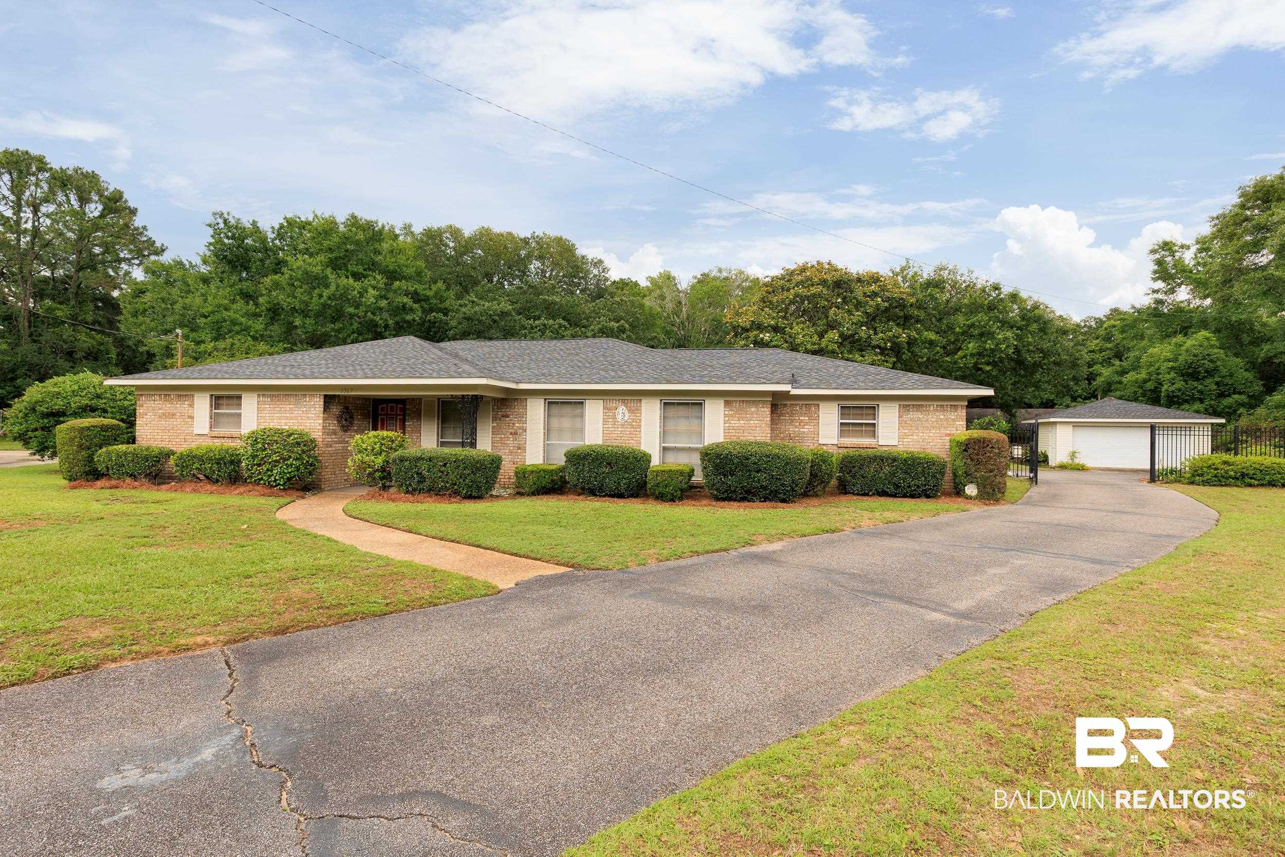 1367 Spring Valley Court Mobile, AL 36693 - Photo 22 of 29 Brick facade home featuring a dark gray shingle roof, established landscaping, a curved sidewalk, and a detached garage with a white door