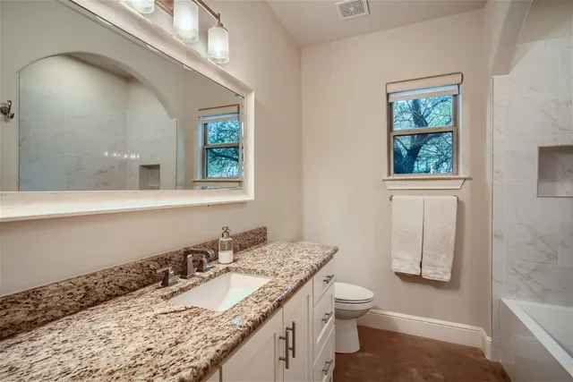 a bathroom with a granite countertop sink a toilet and a mirror