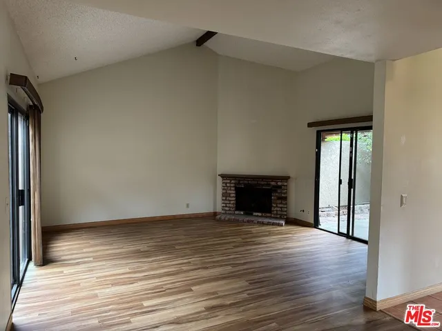 a view of an empty room with wooden floor fireplace and a window