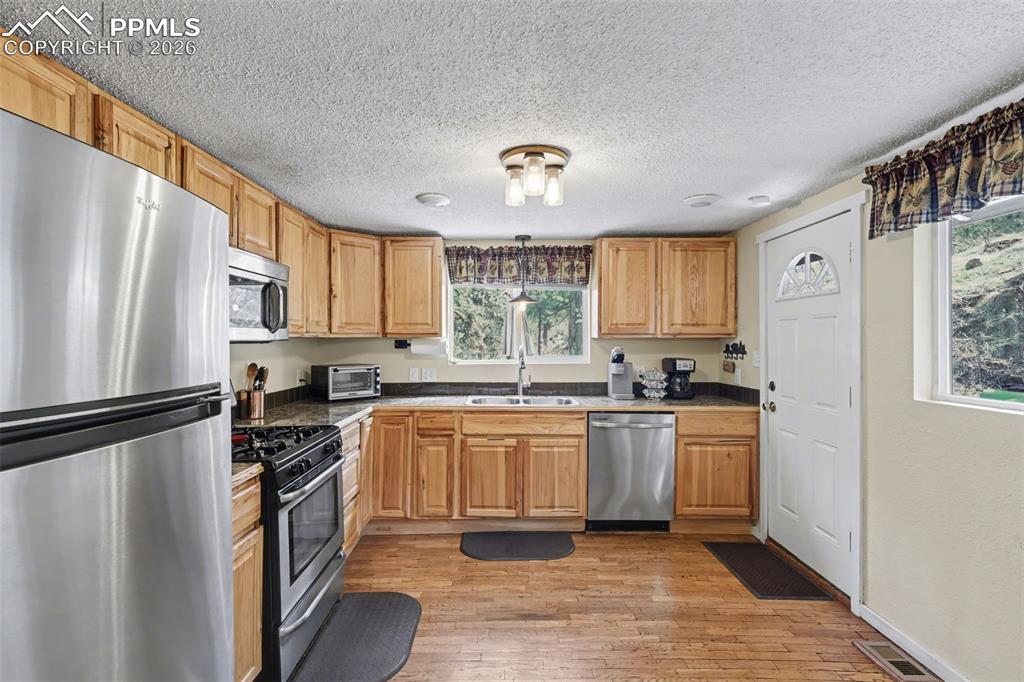 10145 Chipita Park Road Cascade, CO 80809 - Photo 11 of 33 Kitchen featuring stainless steel appliances, light wood-type flooring, dark countertops, decorative light fixtures, and a textured ceiling