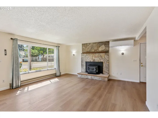 a view of an empty room with wooden floor fireplace and a window