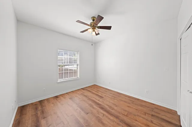 an empty room with wooden floor a ceiling fan and windows