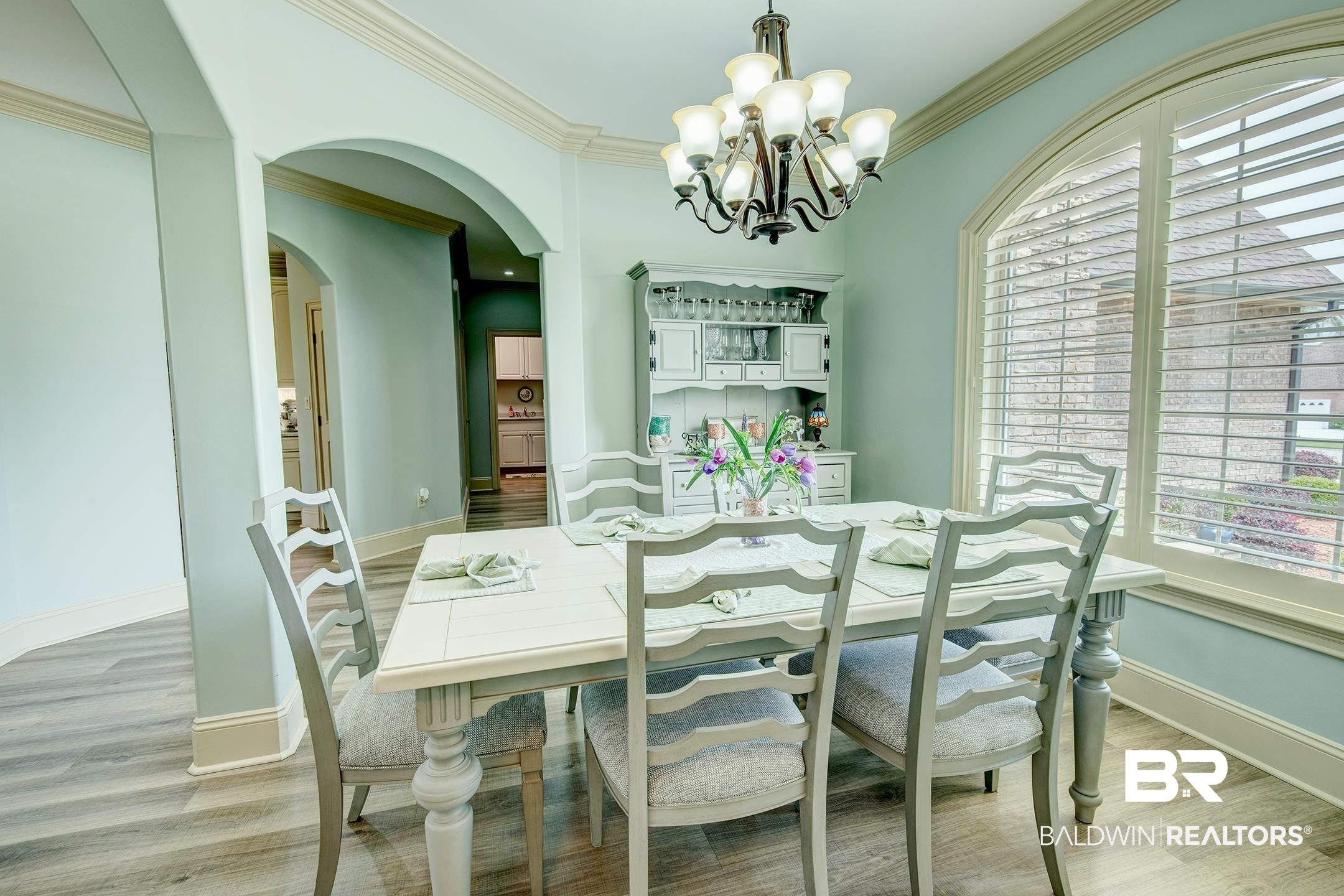 9357 Lakeview Drive Foley, AL 36535 - Photo 28 of 68 Dining area featuring wood-finish flooring, a decorative chandelier, arched window with plantation shutters, crown molding, and an arched entry